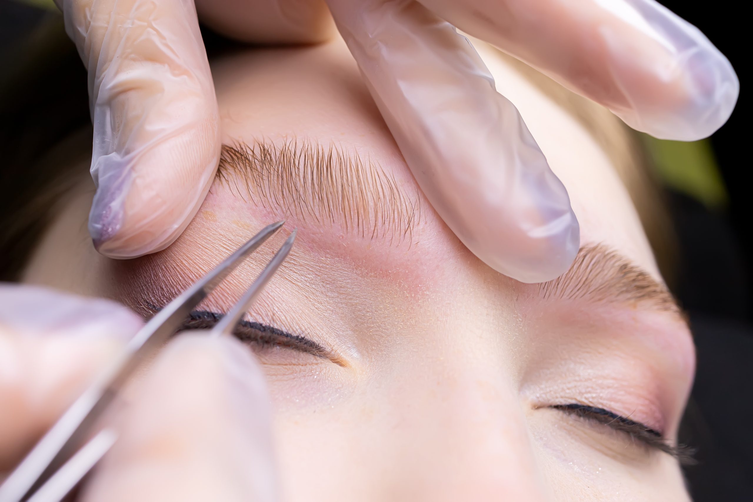 macro photography of the laid eyebrows with the help of lamination, the master tweezers pluck the contour of the eyebrows from excess hairs