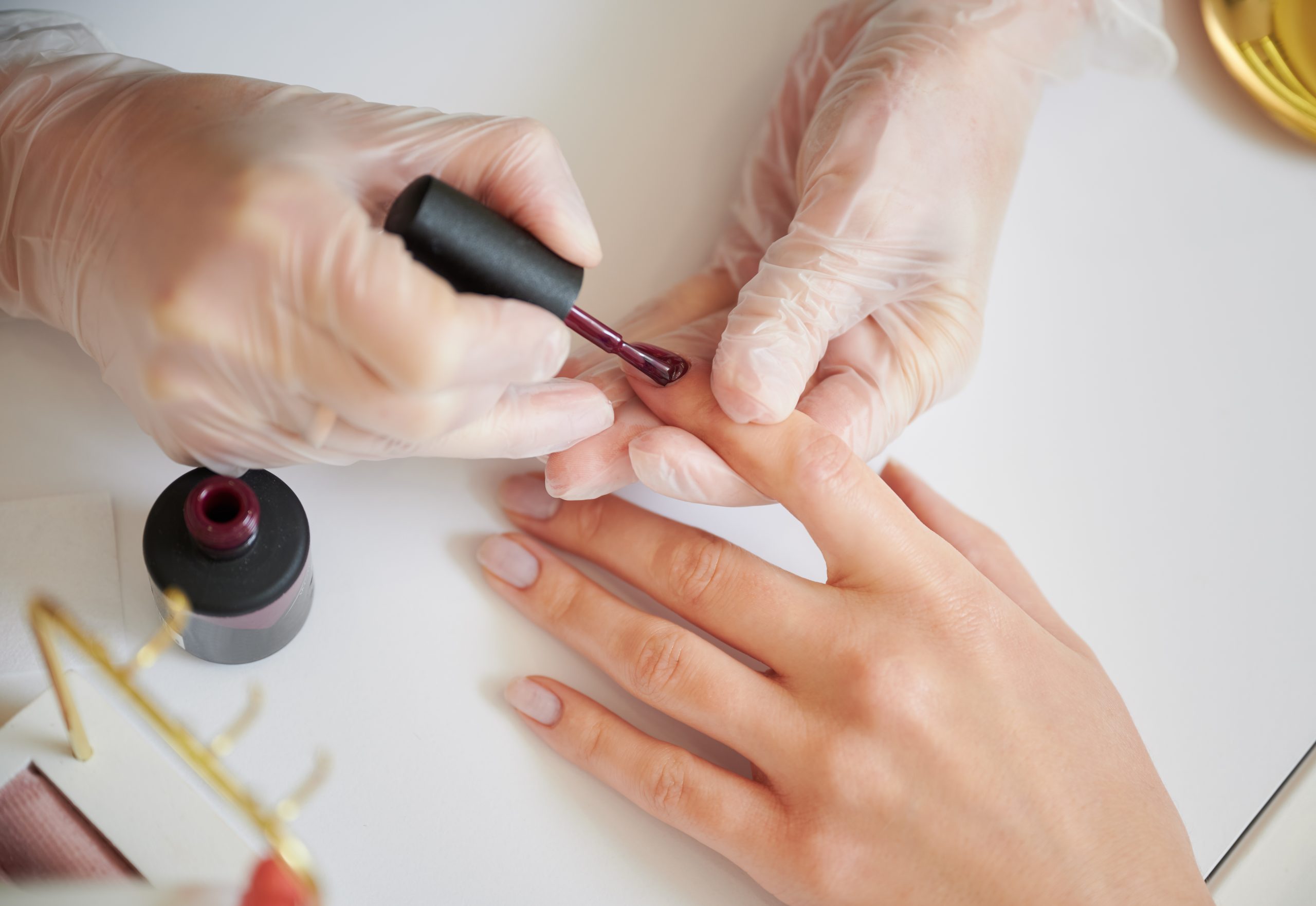 Close up of manicure specialist hands in sterile gloves applying red nail polish on woman fingernail. Professional manicurist doing manicure for female client in beauty salon.